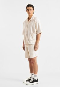Licht beige shirt met korte mouwen en bijpassende shorts met een gestructureerd golfpatroon. Gemaakt met zwarte sneakers en witte sokken.