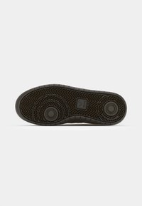Black rubber shoe sole with a herringbone pattern, circular accents, and textured edges. Features a logo imprint and rounded design details.