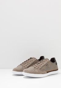 Sneaker in suede e tessuto grigio con dettagli marroni, suole in gomma bianca e cuciture tonali. Design con lacci e dettagli in materiale testurizzato.