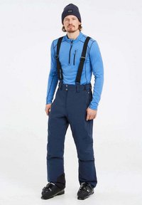 Skiavimo įranga: mėlynas ilgomis rankovėmis viršus, juodos petnešos ir tamsiai mėlynos izoliacinės kelnės; aprūpinta užtrauktuko kišene ir slidinėjimo batais.