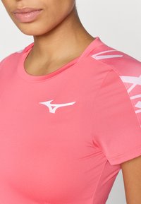 Różowa koszulka sportowa z okrągłym dekoltem, krótkimi rękawami i białym logo na piersi, wykonana z gładkiego, elastycznego materiału.