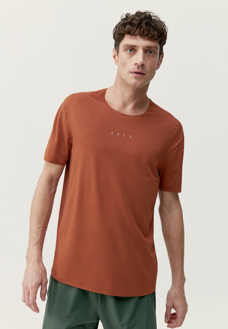 Hrdzavá krátkopytová tričká vyrobené z ľahkého materiálu s okrúhlym výstrihom. Obsahuje jemný detail loga na prednej strane.