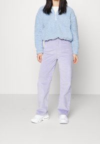 Ljusblå fluffig tröja med kvartsglipa och elastiska muddar, kombinerad med ljuslila manchesterbyxor. Vita sneakers ger en kontrast till outfiten.