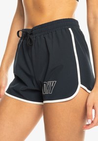 Marineblå idrettsshorts med elastisk midjebånd, snøring og hvit kant. Har en logo trykt på venstre side.