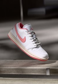 Baskets en cuir blanc avec des accents roses, lacets gris, bout perforé et semelle intermédiaire de couleur crème. Présente un logo rose sur le côté.