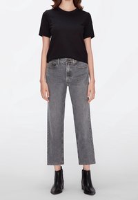 Camiseta de algodón negra de manga corta, combinada con vaqueros gris claros de cintura alta y botas negras hasta el tobillo. Silueta sencilla y de pierna recta.