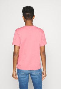 Ljusrosa t-shirt i bomull med korta ärmar, rund halsringning och en liten logotyp vid nackområdet bak. Bärs med blåjeans.