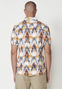 Chemise à manches courtes arborant un motif abstrait coloré dans des teintes d'orange, de bleu et de blanc, avec un col classique et un tissu léger.