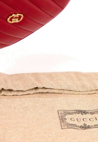 Article en cuir matelassé rouge avec logo double G doré au-dessus d'une pochette en tissu beige étiquetée Gucci.