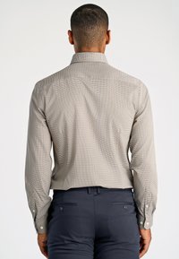 Lichtbruine geruite overhemden met lange mouwen en een klassieke kraag. Voorzien van een knoopmanchet en een nette achterzijde. Gecombineerd met donkere broeken.