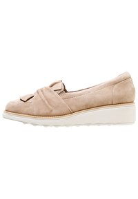 Chaussure slip-on en suede beige avec un détail noué à l'avant et une semelle épaisse blanche avec un léger relief pour une meilleure adhérence.