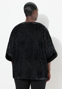 Blusa nera trasparente con motivo floreale in velluto, maniche corte e orlo arrotondato, caratterizzata da una texture morbida e una vestibilità ampia.