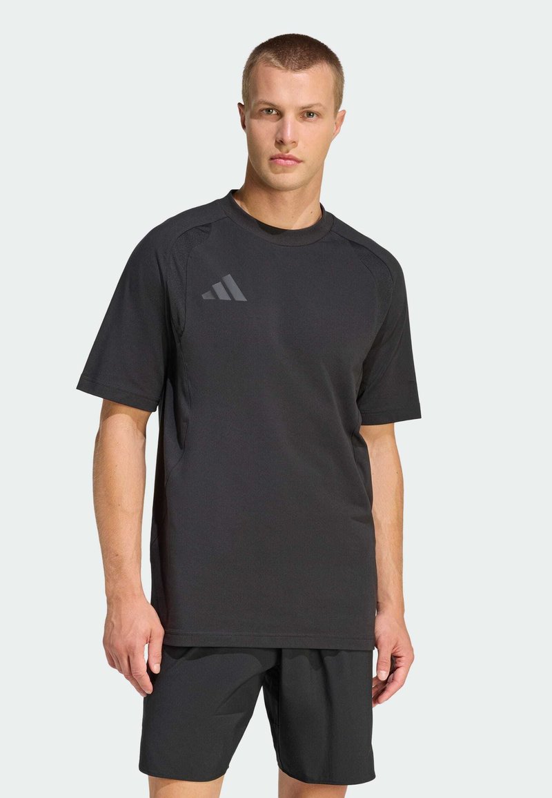 Camiseta deportiva negra de manga corta, con cuello redondo y un logo gris sutil en el pecho, hecha de tela transpirable.