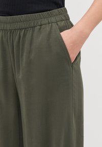 Olivengrønne, lette bukser med elastisk talje, der har sidelommer og en glat, let skinnende overflade.