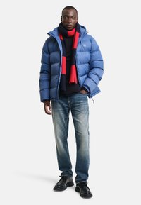 Modrá péřová bunda s kapucí, námořnický svetr, červeno-pruhovaný šátek, džíny a černé boty. Texturovaná tkanina a volný střih.