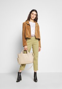 Chaqueta corta de ante marrón, camisa blanca, pantalones verde oliva, botas de tacón negras y un bolso beige. Diseño minimalista con elementos contrastantes.