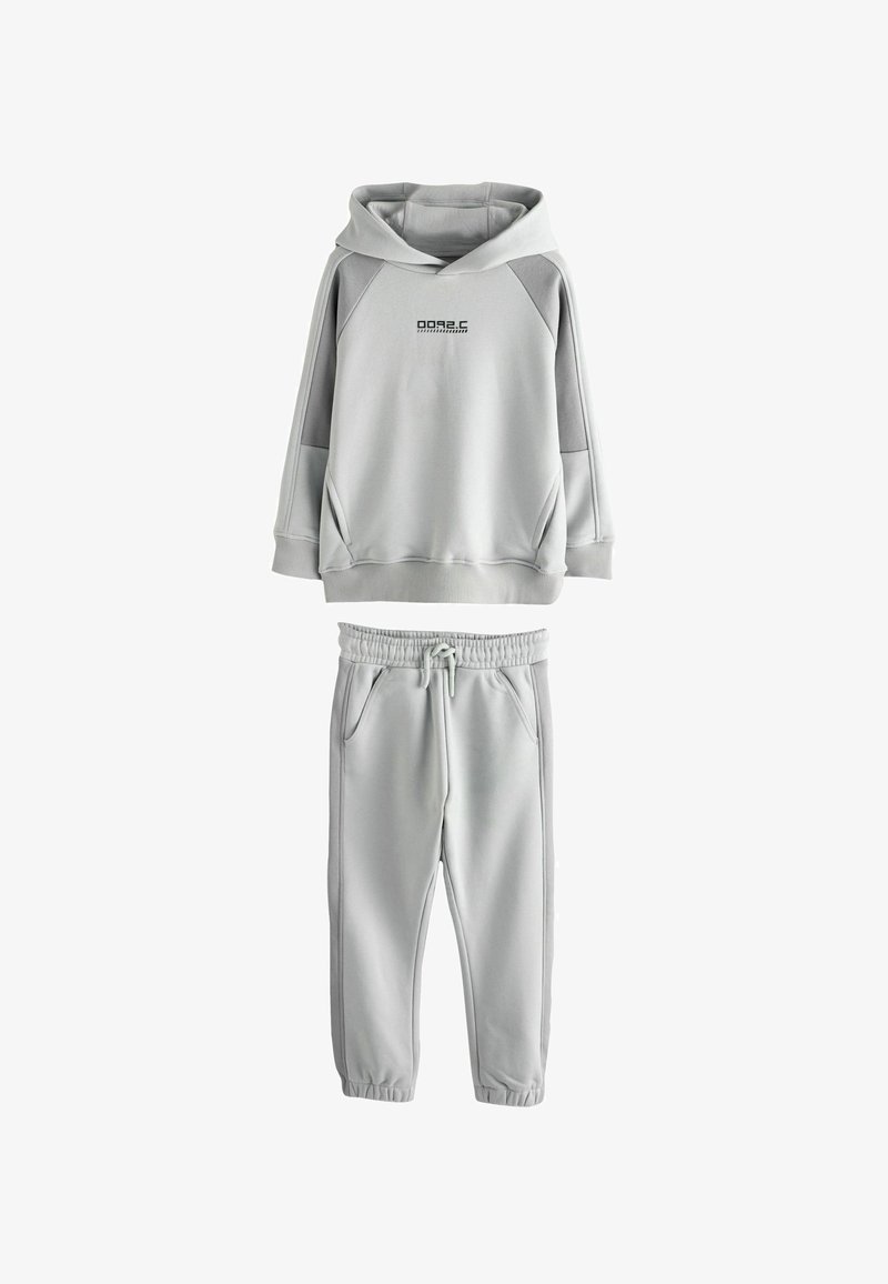 Haut à capuche gris avec une poche frontale et un logo, associé à un pantalon de survêtement assorti avec une taille élastique et des poches latérales.