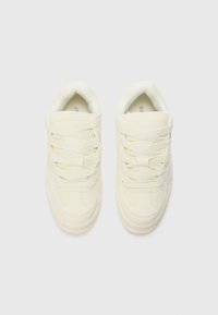 Cream-colored sneakers featuring a smooth leather upper, flat laces, padded collar, and subtle stitching details. Rubber outsole for grip.