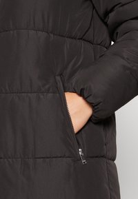 Black puffer jacket featuring a quilted design, visible zippered pocket, and elastic cuffs, made from lightweight, water-repellent fabric.