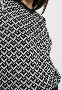 Maglione nero con un motivo geometrico zigzag argento, caratterizzato da un colletto tondo e polsini a costine. Texture morbida, design aderente.