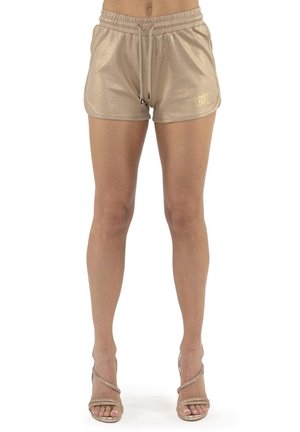 Modèle portant un short beige à cordon de serrage et des sandales à talons hauts à brides, sur fond blanc.