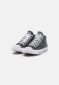 Tenisi negri în stil high-top, fabricați din pânză, cu talpă albă, având un design tradițional cu șireturi, vârf din cauciuc și logo pe limbă.