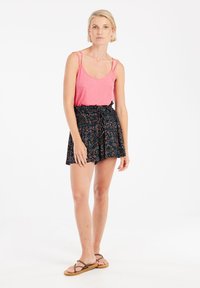 Débardeur rose à fines bretelles associé à un short noir à imprimé floral, avec une taille smockée et un détail de nœud. Sandales à lanières marron.