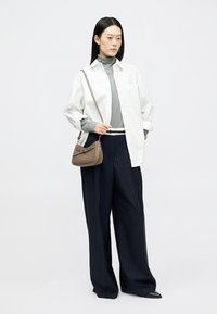 Bílá volná košile, šedý rolák, tmavě modré široké kalhoty s proužky a malá hnědá kabelka; elegantní design s neutrálními tóny.