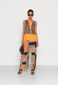 Óculos de sol pretos, blusa sem mangas com estampado laranja e de leopardo, e calças largas com estampados de animais. Acessórios incluem uma bolsa preta.