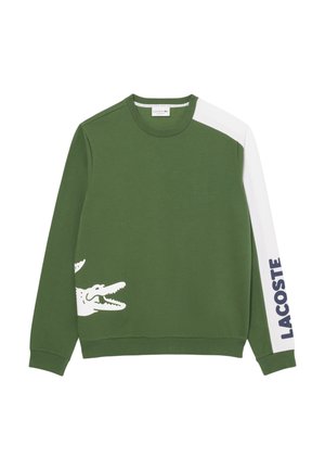 Zielony sweatshirt wykonany z mieszanki bawełny, z białą wstawką na jednym ramieniu, z dużą białą grafiką krokodyla i napisem "LACOSTE" w kolorze granatowym.