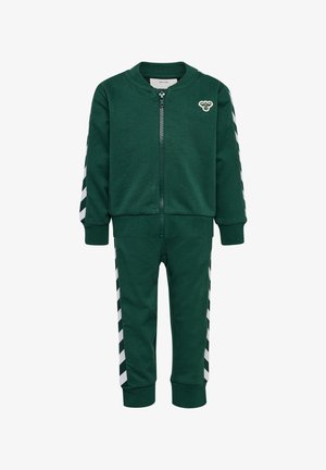 Grön zip-up jacka och matchande byxor i bomull. Jackan har vita chevron-ränder på ärmarna, med en liten logotyp på vänster bröst.