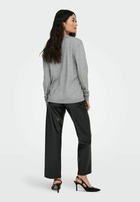 Grauer Langarmpullover mit gerippten Bündchen, kombiniert mit schwarzen, weiten Hosen aus Kunstleder und spitzen schwarzen Absatzschuhen.