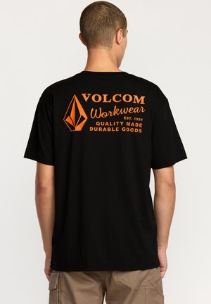 T-shirt en coton noir avec un logo graphique orange au dos, affichant "VOLCOM Workwear" et "Produits durables de qualité fabriqués."
