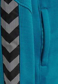 Primo piano di tessuto blu strutturato con una banda a spina di pesce verticale bianca e nera e una tasca verticale con fessura.