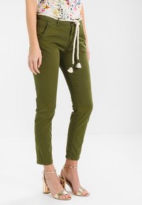 Olivgröna byxor med dragsko, med fransar i ändarna. Bärs tillsammans med metalliska klacksandaler. Enkel, slim fit-design.