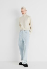 Cream turtleneck sweater with ribbed hem paired with light blue high-waisted jeans and black shoes, against a plain white background.