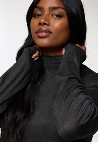 Dopasowany ciemnoszary golf z długimi rękawami. Gładka tekstura, minimalistyczny design, z otworami na kciuki na końcach rękawów dla większego komfortu.