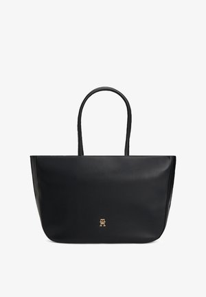 Zwarte leren totebag met twee handvatten en een klein goudkleurig logo-embleem centraal geplaatst vlak bij de onderkant.