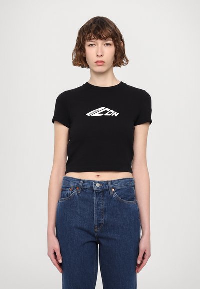 T-shirt noir raccourci à manches courtes, avec un logo imprimé blanc sur la poitrine. Associé à un jean en denim bleu taille haute.