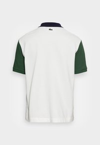 Vit pikétröja med gröna korta ärmar och krage i marinblått. Har en liten broderad logotyp på nacken. Mjuk bomullsmaterial.