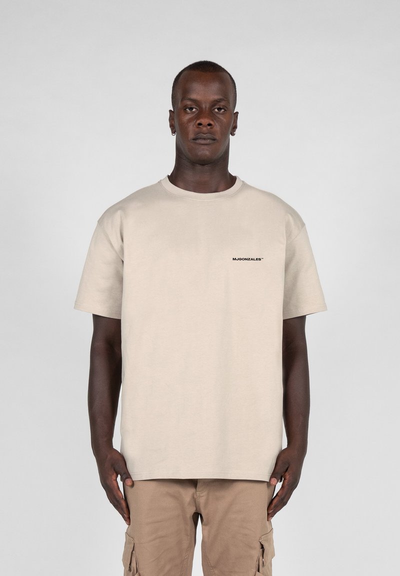 Tricou din bumbac bej, cu guler rotund și mâneci scurte; are un logo negru pe pieptul stâng. Purtați cu pantaloni cargo bej.