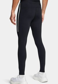 Leggings sportivi neri con una texture liscia, dotati di tasche laterali con zip e strisce bianche sui bordi esterni. Design aderente.