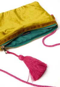 Borsa a mano in velluto gialla con foderatura turchese, zip dorata e tracolla intrecciata rosa con un grande pompon rosa.