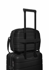 Schwarzer Hartschalenkoffer mit kleiner Tragetasche oben. Ausgezogene Teleskopgriff, verstellbarer Riemen sichert die kleinere Tasche, strukturierte Oberfläche, Reißverschlussabschluss.