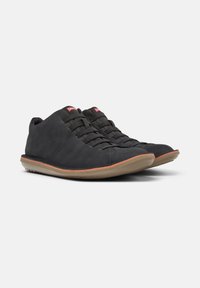 Sneaker nere eleganti con una finitura liscia, dotate di sei occhielli per i lacci e una suola in gomma color tan a contrasto, posizionate su uno sfondo neutro.