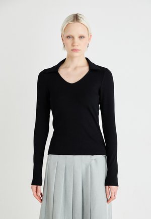 Black ribbed long-sleeve top with a V-neck and structured collar, paired with a pleated light gray skirt, featuring a side detail.