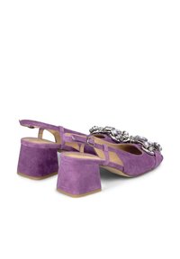 Zapatos de tacón de ante morado con tiras traseras y un tacón cuadrado grueso, que presentan una cadena decorativa de piedras brillantes en la parte delantera. Textura suave y diseño abierto.