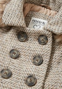 Beige fiskbensmönstrad kappa med en mjuk textur, utrustad med fyra rundade knappar och en ljusbrun innerfoder. Etiketten säger "ORIGINAL LIMITED EDITION."