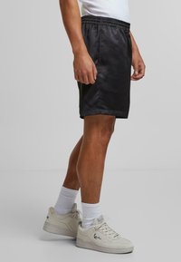 Sorte satin atletiske shorts med elastisk talje, knælangt snit og glat tekstur, parret med hvide atletiske strømper og sneakers.