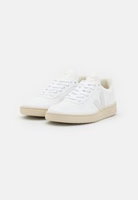 Hvide sportssko med perforerede detaljer, beige sål, flade snørebånd og logo på tungen, som har et minimalistisk design og er lavet af læder.